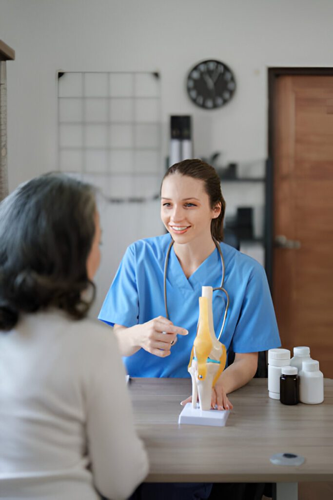 Medical professional in blue scrubs explaining knee joint anatomy model to patient during consultation