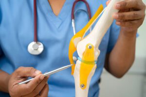 Medical professional in blue scrubs pointing to specific areas on knee joint model with surgical instrument