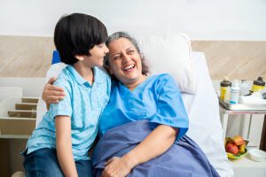 Young boy in light blue polo shirt visiting patient in hospital room, medical supplies visible on bedside table with fresh fruit