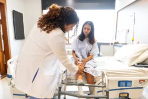 Healthcare provider performing a knee reflex examination on a patient in a hospital gown