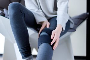 Person wearing gray athletic wear applying a black knee brace for meniscus support