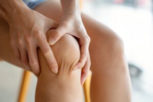 Close-up photograph of hands holding a painful knee, demonstrating common meniscus injury symptoms.