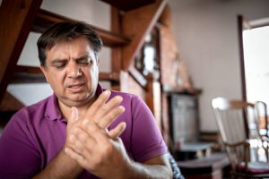 Person in purple polo shirt examining hand pain with concerned expression in home setting