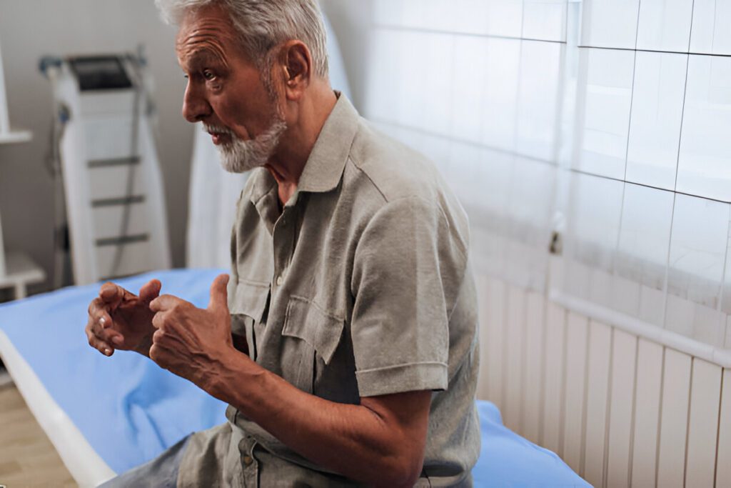 Elderly patient in medical setting demonstrating hand movement during recovery consultation