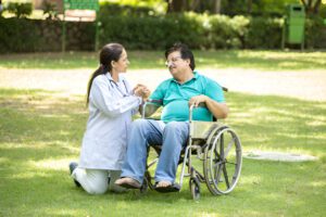 Healthcare provider kneeling beside patient in wheelchair during outdoor therapy session in garden setting