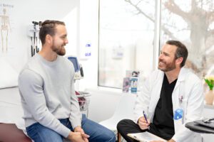 Medical consultation between doctor and patient in clinical setting with skeletal diagram visible on wall