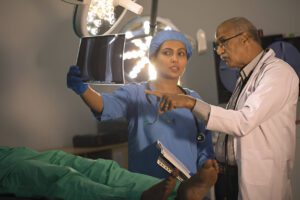 Medical professionals reviewing X-ray images in a clinical setting, with surgical lights visible overhead.