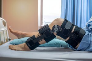 Patient wearing black adjustable hinged knee brace on hospital bed with blue curtain background