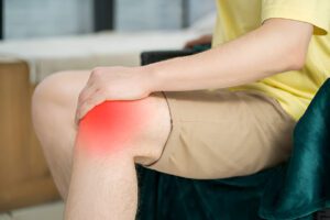 Person in yellow shirt touching inflamed knee area shown with red highlight"